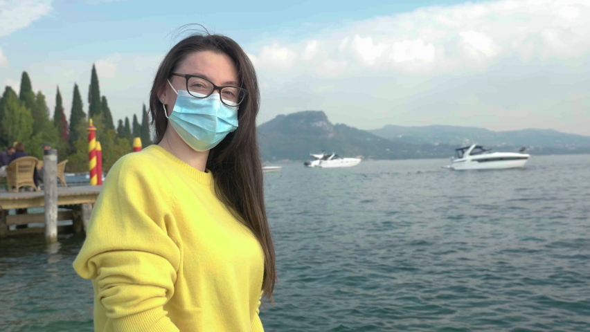Slow motion shot of young, beautiful woman with glasses removing her protective mask, scenic landscape