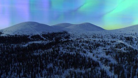 Aerial view of colorful Aurora Borealis, the Northern lights above Tunturi fell mountains, winter dawn, in Northern Scandinavia - dolly, drone shot