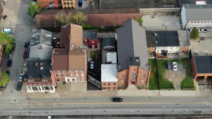 Aerial of city buildings in run-down part of town. Overhead top down shot of church, brick home, boarded-up apartment low-income housing. Cars and traffic pass by on street.