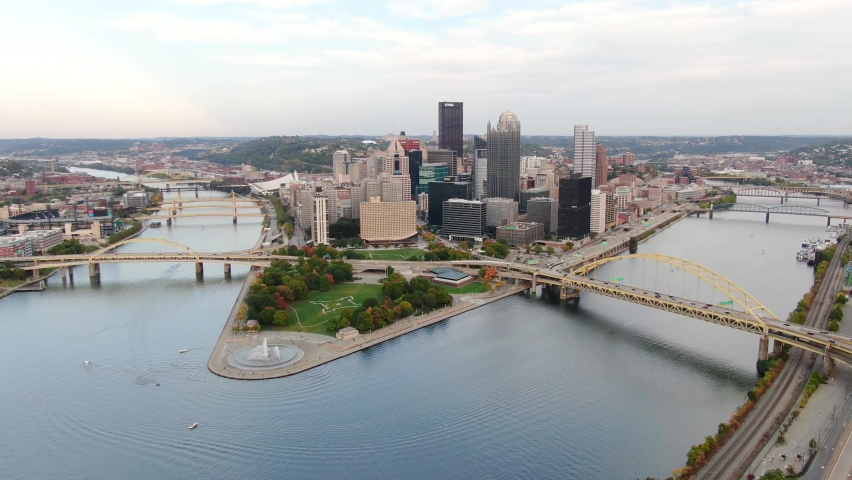 Wide aerial establishing shot of Pittsburgh Pennsylvania. Point State Park and boats on Allegheny and Monongahela Rivers. Drone above Mount Washington. City of Bridges. Royalty-Free Stock Footage #1061401444