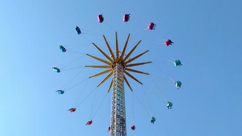 Vertical colorful chain fair swing spinning people around, symmetrical minimal background blue sky, static