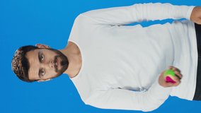 Young man playing with small colored ball. Blue background. Slow motion video.Video for the vertical story.