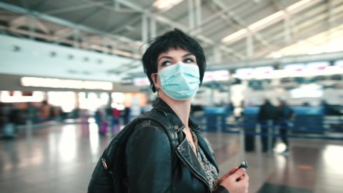 A woman in mask stands in an empty airport, looks around, tries to navigate. Cancellation of aircraft during the COVID-19 pandemic. Circular movement camera. Lockdown over Omicron variant.