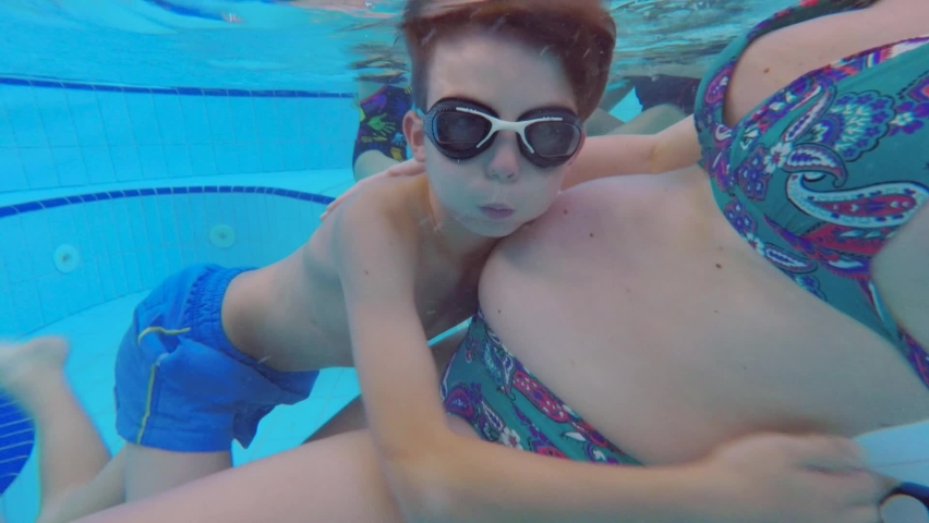 Teenager hugs pregnant mother underwater in pool, water procedures. Leisure activities with family on weekends. Psychological contact. Emergence hormone oxytocin, communication with mother. | Shutterstock HD Video #1061412607