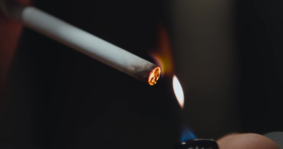 Close up of person lighting cigarette from lighter and smoking, dark background