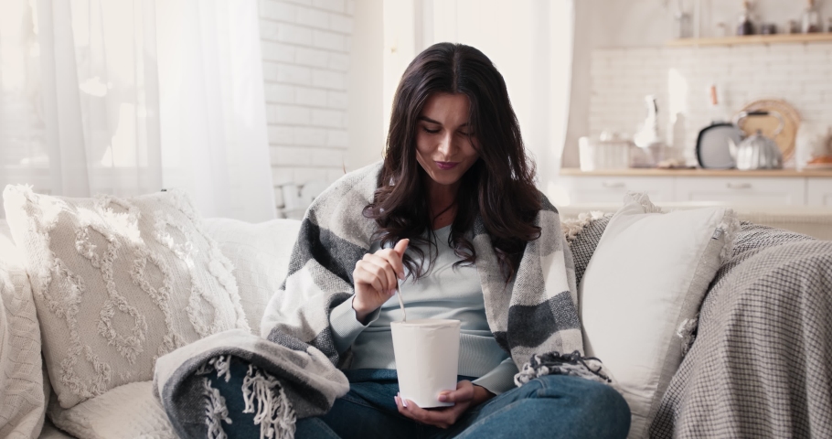 Female treatment against depression. Cheerful young lady enjoying ice cream, laughing while sitting on couch wrapped in plaid Royalty-Free Stock Footage #1061412730