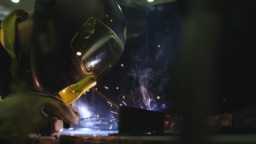 Factory worker welds metal. The man is welding. Welding with argon or electrode, using a welding machine. An industrial enterprise producing metal structures. Sparks and flashes fly. Slow motion | Shutterstock HD Video #1061414041