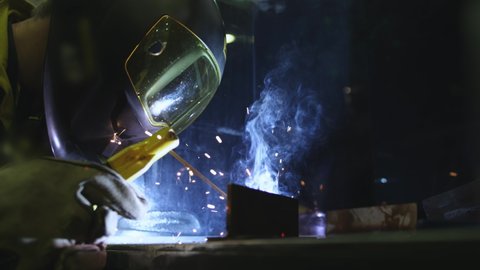 Factory worker welds metal. The man is welding. Welding with argon or electrode, using a welding machine. An industrial enterprise producing metal structures. Sparks and flashes fly. Slow motion