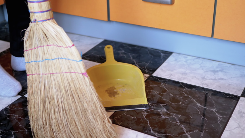 A woman sweeps the tile floor with an old broom and shovel in a modern kitchen. A woman in white socks with a broom in her hands. Sweep the floor. 4K | Shutterstock HD Video #1061415028
