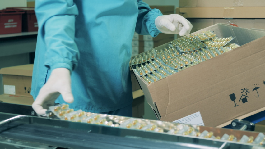 Pharmacist puts pills into a box. Pharmaceutical factory production line. Pharmaceuticals production line at a modern pharmaceutical facility. Royalty-Free Stock Footage #1061415997