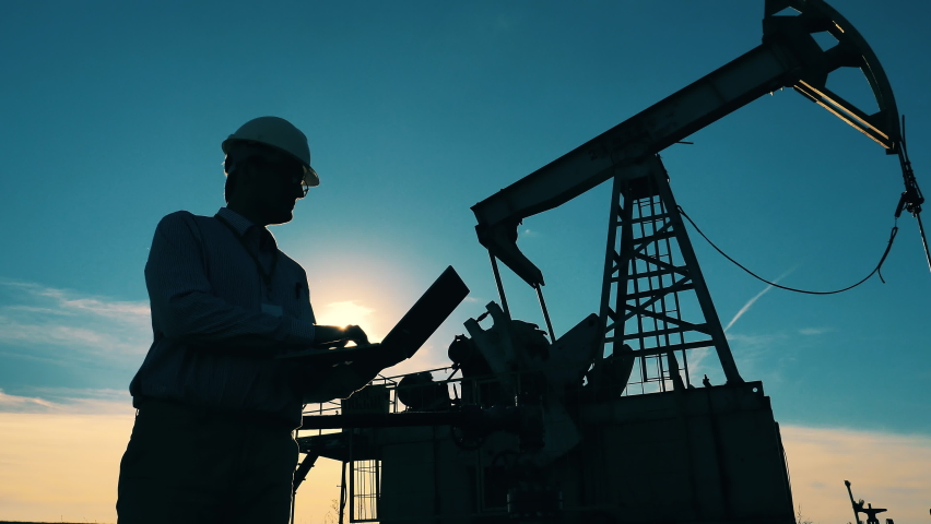 Silhouette of an oil worker and an oil pump. Oil industry, crude oil prices concept. Royalty-Free Stock Footage #1061416117