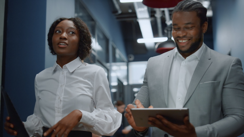 Closeup african american colleagues walking in business center. Positive afro business couple discussing plan on tablet computer in office. Successful business people working on the go in corridor Royalty-Free Stock Footage #1061418457