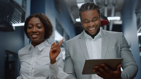 Closeup african american colleagues walking in business center. Positive afro business couple discussing plan on tablet computer in office. Successful business people working on the go in corridor