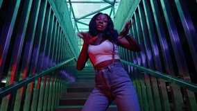 Girl Dancer Dancing On The Stairs. Black Young Girl Moves Rhythmically. She Has Long Black Hair. Pretty Dancer. Facial Expressions Of The Girl Change Guickly. Lighting Creates Blue And Green Colors
