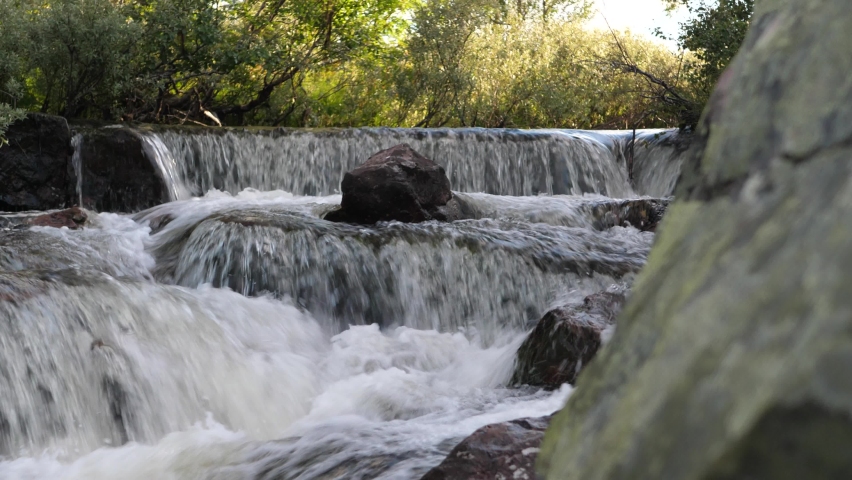 Low angle close up lurking behing rock showing downstream of Njupeskärs waterfall cascading down rocky steps, in Fulufjällets National park, Sweden
