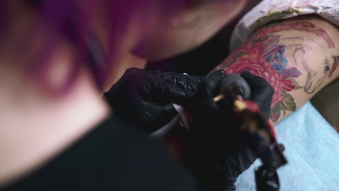 A close-up of a tattoo artist makes a pink unicorn on a female arm. Professional tattooist working with sterile instrument and in gloves. LGBT symbol. Body art, tattooing, creative design concept.