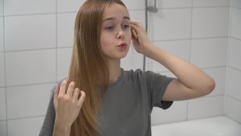 Attractive happy confident young beautiful young woman brushing healthy long hair with wooden hairbrush looking in the mirror. Teenage girl doing hairstyle in bathroom in the morning at home get ready