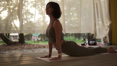 Fit woman is doing yoga in wooden hut filled with light, the girl performs yoga stands and elements