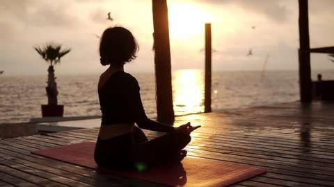 Yogi girl is sitting in lotus pose in front the sea in summer on sunset and meditating