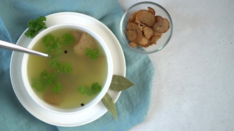 A woman's hand adds bay leaf to a bowl of broth. Parsley leaves and croutons. Broth helps strengthen the immune system. Collagen for joints. Top view. Horizontal orientation.