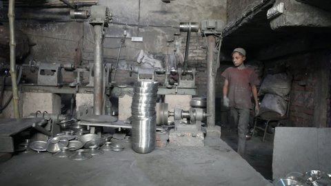 DHAKA, BANGLADESH - OCTOBER 25, 2020: A dark sweatshop garage where underaged childlabor workers are busy pressing steel plates in the aluminium factory under unhealthy and dangerous circumstances