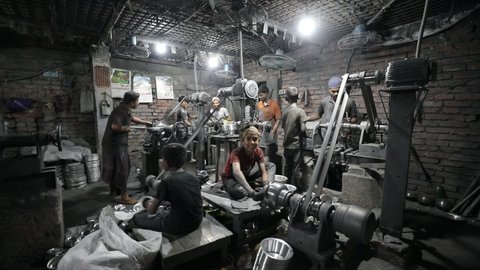 DHAKA, BANGLADESH - OCTOBER 25, 2020: A dark sweatshop garage where underaged childlabor workers are busy pressing steel plates in the aluminium factory under unhealthy and dangerous circumstances
