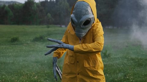 aliens dance in smoke. alien has arrived on earth and is standing in forest. an actor in alien costume, in yellow raincoat and khaki pants, touches his hands.UFO futuristic concept