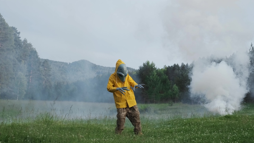 Aliens dance in smoke. alien has arrived on earth and is standing in forest. an actor in alien costume, in yellow raincoat and khaki pants, touches his hands.UFO futuristic concept | Shutterstock HD Video #1061432275