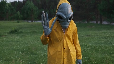 alien waved his hand and welcomed.alien has arrived on earth close up.an actor in alien costume, in yellow raincoat and khaki pants, touches his hands.UFO futuristic concept