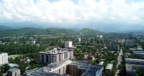 Top view of Almaty city. Green streets, big clouds and tall houses. Summer day, traffic on the roads is small, sometimes you can see high mountains. People go about their business. Beautiful city.