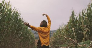 Slow motion of Caucasian woman, from the back wearing yellow shirt, walking in a corn field. Feeling happy, realized. Dreaming picture of Happiness, freedom, calmness.