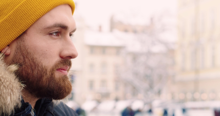 Close up of young bearded tourist in winter clothes making photo of city on camera. Winter travel.