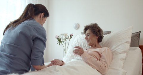Nurse Administering Medications to Female Senior Patient. Cheerful Home Caregiver Giving Pills to Elderly Female Patient Lying in Bed.