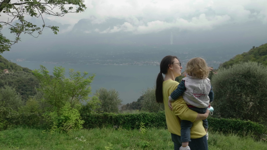 Young mother showing her toddler son the beautiful, majestic mountains in a scenic landscape, Garda Lake