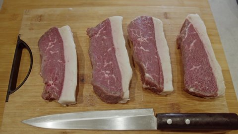 Four meat steaks and kitchen knife on top of wooden cut board. Cooking Brazilian Picanha. Close up.