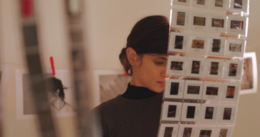 Female photographer holding diapositives or frames of slide film in darkroom. Portrait of creative girl photographer in photo studio darkroom. Developing analog camera film.