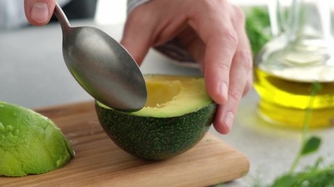 Scooping avocado flesh with a spoon. Male chef scoop avocado pulp. Cooking healthy food