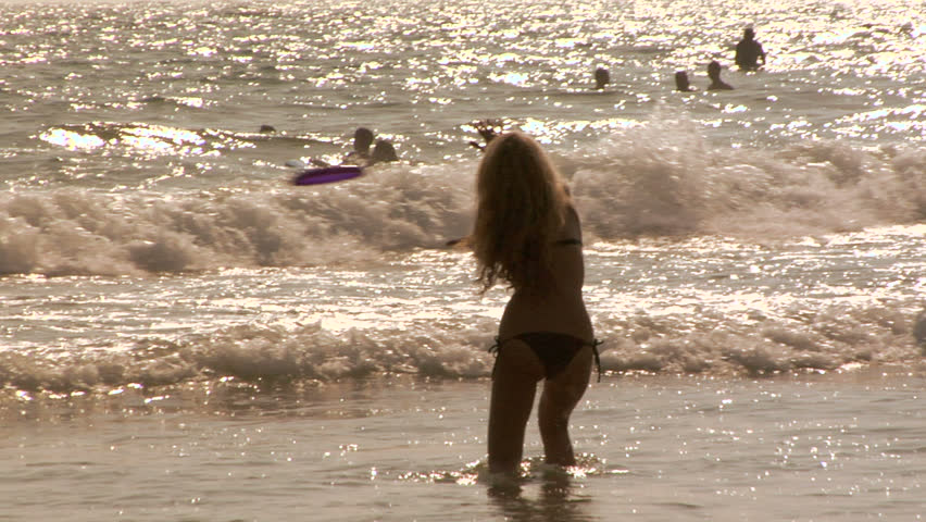 Girl in bikini throws frisbee at Huntington Beach, CA in the summertime in slow