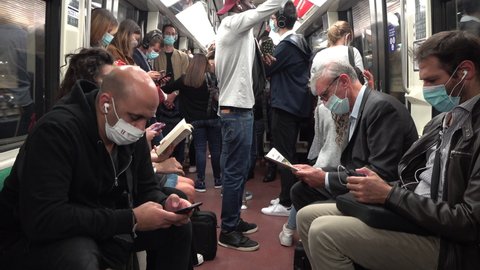 PARIS, FRANCE – SEPTEMBER 2020: Metro passengers wear face masks in Paris. A senior man reading a newspaper contrasts with younger people using their smarthpone. Covid-19 coronavirus pandemic.