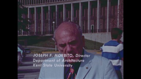 1970s: Man stands outside building, talks.