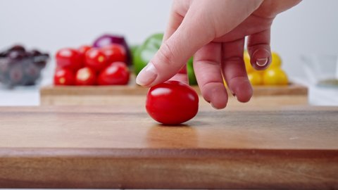 A close-up look of woman's hand spinning Cherry Tomatoes on cutting board in slow-motion, 4K with vegetables in background.