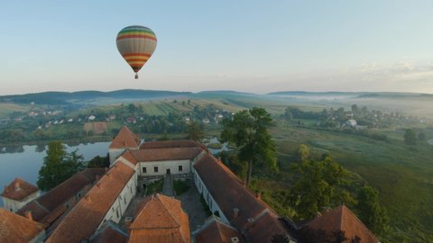 Colorful hot air balloons fly over the medieval castle and lake in the morning fog. Maneuverable flight. Travel, adventure, festival.