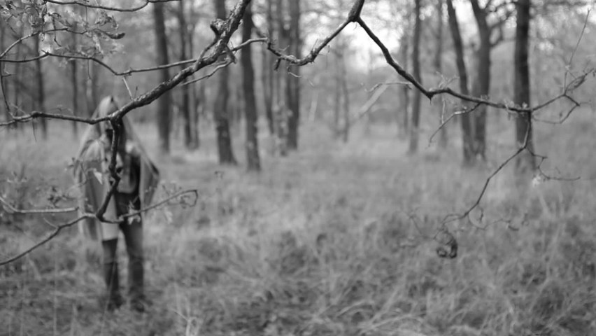 A man wearing a monster mask freak with a blanket on his head walks through the woods. Halloween.Black and white video.
