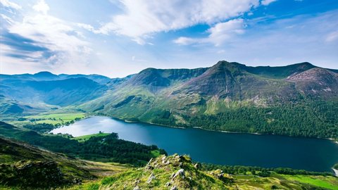 Clouds rolling over Buttermere lake and scenic mountain valley in Lake District, Cumbria, UK on sunny summer day.View from high up.Idyllic landscape scenery.4K nature time lapse video clip.