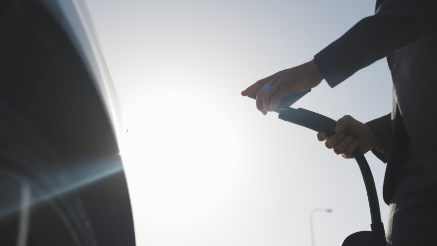 Unrecognizable businessman plugging electric car from charging station. Senior is plugging in power cord to an electric car at sunset. Caucasian businessman charging electric car at charging station Royalty-Free Stock Footage #1061468395