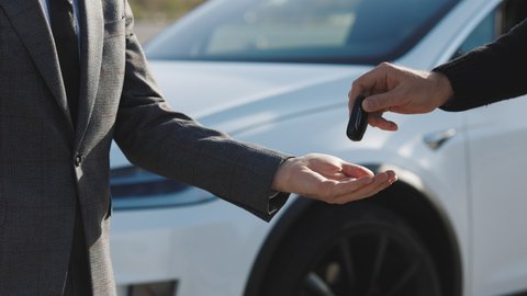 Male hand gives a car keys to male hand in the car dealership close up. Unrecognized auto seller and a man who bought a vehicle shake hands. Dealer giving key to new owner in auto show or salon.