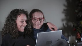 People, technology and friendship concept - happy teenage girls with laptop sitting on sofa and having video call at home