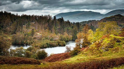 Tarn Hows in autumn.Clouds rolling over hills with trees and lake.Mountain peaks in background.Idyllic landscape scenery in Lake District, Cumbria, UK.4K nature time lapse video clip.