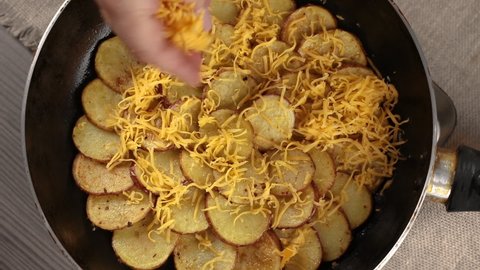 adding cheddar cheese into a frying pan with sliced potatoes, top view. concept of homemade cooking