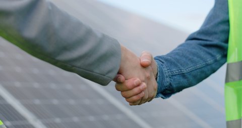 Close up of handshake on solar panel background outside. Female engineer shakes hands with partner in agreement.